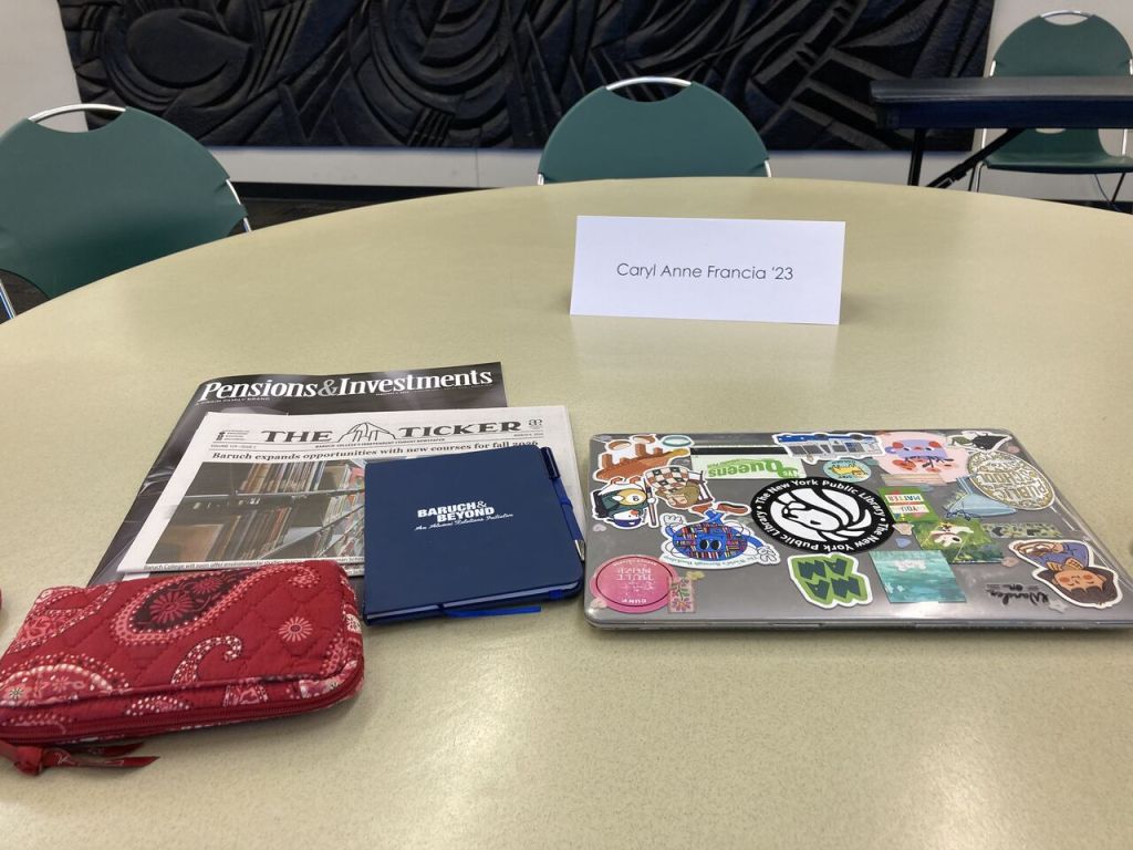Caryl Anne Francia's laptop, newspapers and belonging sit on top of a table with her nameplate at Baruch College.